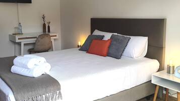 A neatly made bed with white bedding, a grey throw blanket, and a small bedside table with a lamp.