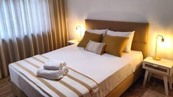 A neatly made bed with white and striped bedding, two bedside lamps, and a window with curtains.