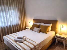 A neatly made bed with white and striped bedding, two bedside lamps, and a window with curtains.
