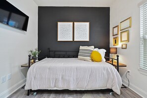 Un dormitorio con una cama, una mesita de noche, una lámpara y cuadros en la pared.