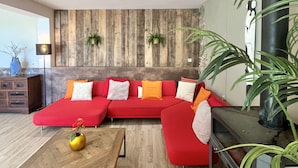 A modern living room with a red sectional sofa, a wooden coffee table, and a large black fireplace. - Domaine de La Blache - La Bergerie (Saint-Jurs)