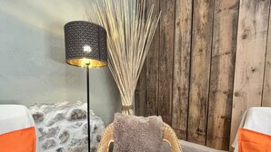 A room with a wicker chair, a floor lamp, and two white sofas with orange cushions. - Domaine de La Blache - La Bergerie (Saint-Jurs)