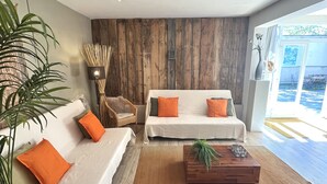 A modern living room with a white sofa, orange cushions, a wooden coffee table, and a large plant. - Domaine de La Blache - La Bergerie (Saint-Jurs)