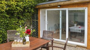 Une table en bois placée à l’extérieur, avec des chaises, un vase de fleurs et des verres à vin.
