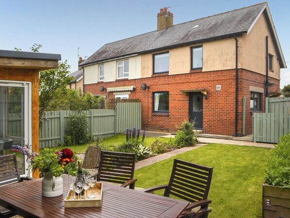 A residential property with a garden, a wooden table with chairs, and a brick house.