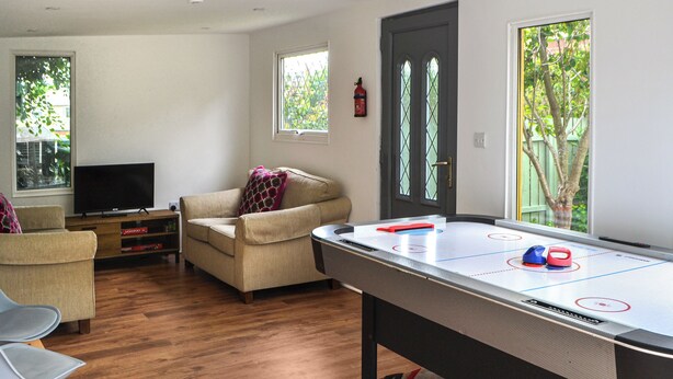 Un salon avec une table de billard, un canapé, un téléviseur et une fenêtre donnant sur les arbres.