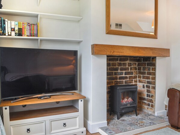 A living room with a television on a wooden stand, a fireplace with a brick surround, and a bookshelf with books.