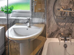 A bathroom with a sink, a shower, and a potted plant by the window.