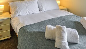 Un lit bien fait, avec des draps blancs, une couverture grise et deux serviettes blanches pliées posées sur le lit.