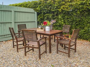Une table en bois avec six chaises, un vase rempli de fleurs et une bouteille posée sur un plateau.