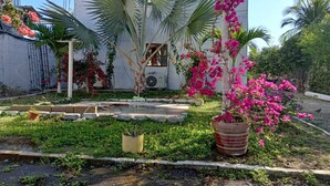 Zona residencial con un edificio blanco, palmeras y un jardín con flores rosadas.