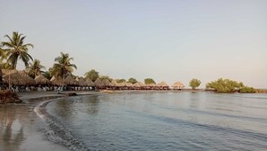 Una playa con cabañas de techo de paja y palmeras.