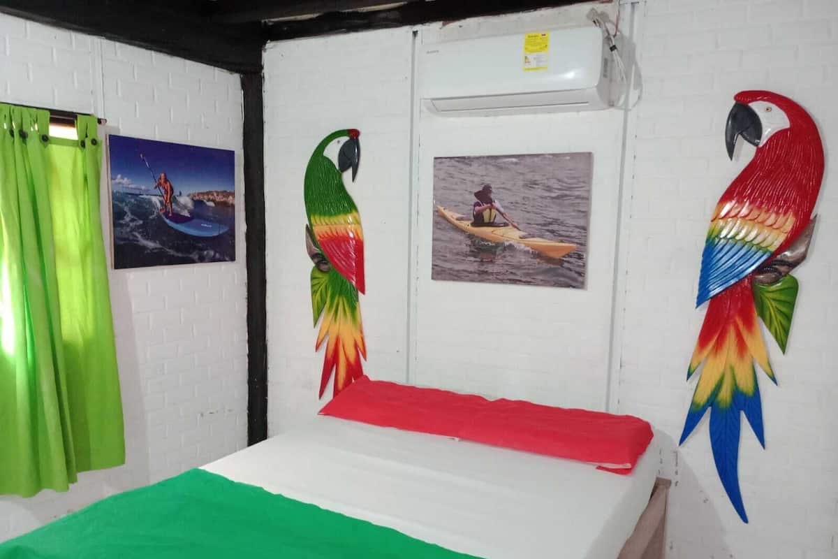 A room with a bed, a green curtain, a wall-mounted air conditioner, and two wall decorations of birds.