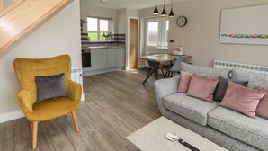 A modern living room with a sofa, armchair, and coffee table. A staircase leads to an upper level. - Bwthyn Cae'r Efail (Rhosgoch)