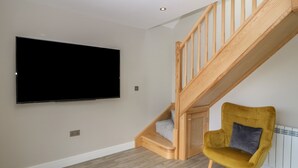 A room with a wooden staircase, a flat-screen TV mounted on the wall, and a mustard-colored armchair with a cushion. - Bwthyn Cae'r Efail (Rhosgoch)