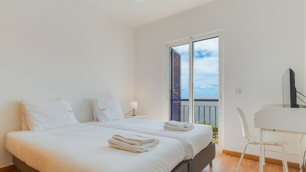 A modern hotel room with a large bed, a desk, and a view of a building through a balcony door. - Esfera I (Santa Cruz)