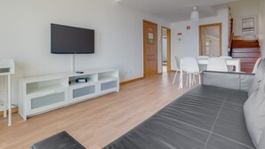 A modern living room with a flat-screen TV, white entertainment unit, grey sofa, and a staircase leading to another level. - Esfera I (Santa Cruz)