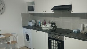 A compact kitchen with a washing machine, microwave, and a small dining area with a chair. - Le Petit Viry, à 20min D'orly (Viry-Châtillon)