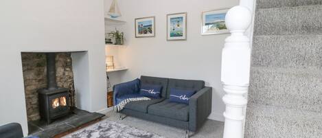 A living room with a stone fireplace, grey sofa, and a staircase.