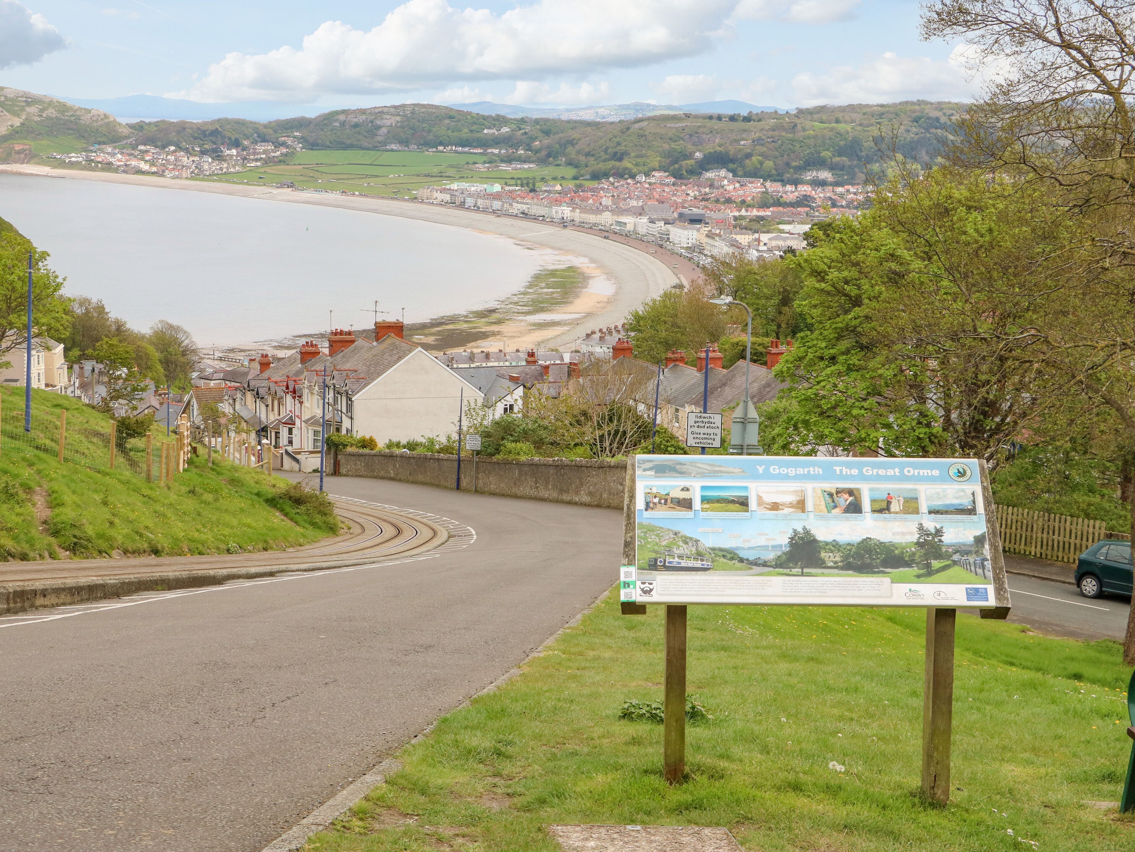 A coastal road with a signboard and a view of a town and beach.