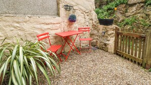 A small outdoor seating area with red metal chairs and a table, surrounded by pebbles and plants. - Pebblestone Cottage (Llandudno)