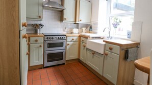 A kitchen with white cabinets, a stove, and a window. - Pebblestone Cottage (Llandudno)