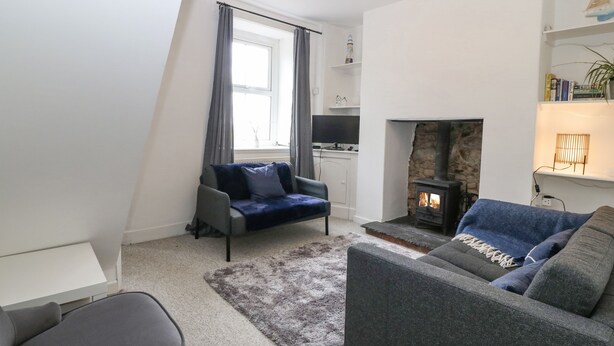 A modern living room with a fireplace, two sofas, a TV, and a bookshelf. - Pebblestone Cottage (Llandudno)