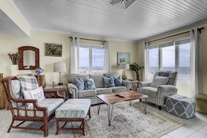 A spacious living room with a view of the sea, featuring a sofa, armchairs, a coffee table, and a rug.