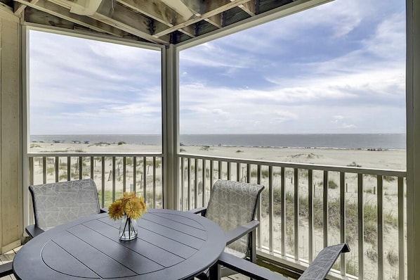A covered outdoor seating area with a table and chairs, overlooking a beach.