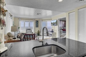 A modern kitchen with a granite countertop, stainless steel sink, and a view of the ocean through large windows.