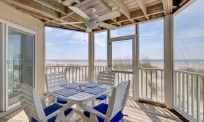 A covered outdoor seating area with a table and chairs, overlooking a beach.