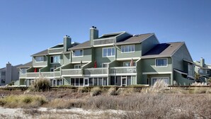 Un immeuble à plusieurs étages situé en bord de mer, doté de balcons et surplombant une plage de sable.