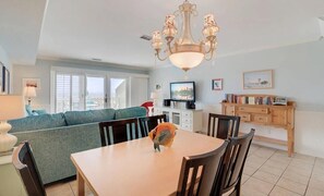 Ein Essbereich mit Tisch, Stühlen, einer Chandelierleuchtre, einer Couch und einem Fernseher.