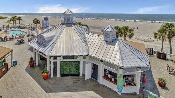 Un edificio frente a la playa con piscina, asientos exteriores y vistas a la playa.