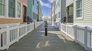 Un muelle de madera entre hileras de casas de pueblo coloridas con barandillas blancas y un cielo despejado.