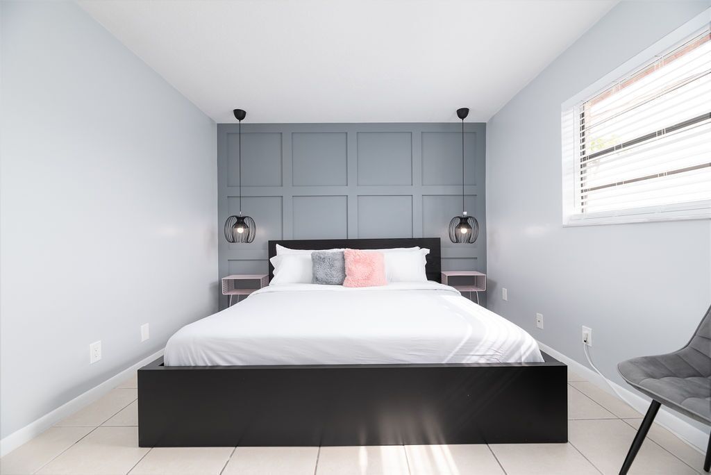 A modern bedroom with a large bed, grey walls, and a window with blinds.