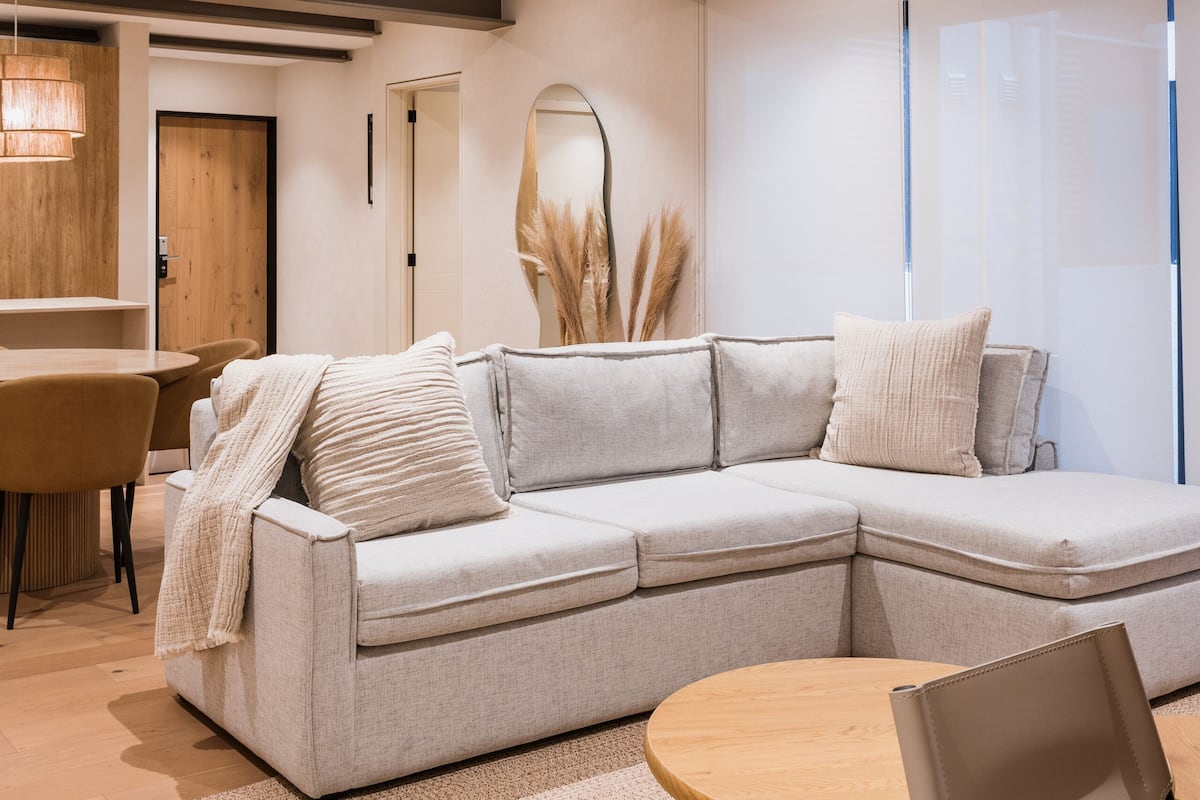 A modern living room with a sectional sofa, a round wooden coffee table, and a dining area with a wooden table and chairs.