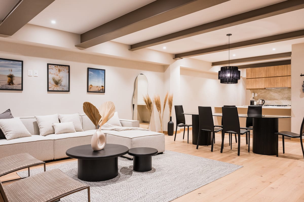 A modern living room with a sectional sofa, round coffee tables, and a dining area with chairs and a table.