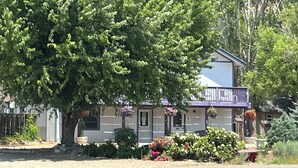 A two-story house with a large tree in front, a balcony on the second floor, and a well-maintained garden with various plants and flowers. - DOWNTOWN DOLORES COLORADO w/river access - Stay at Cozy Comfort Inn, Dolores, CO (Dolores)