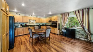 A kitchen with wooden cabinets, a dining table with chairs, and a window with curtains. - DOWNTOWN DOLORES COLORADO w/river access - Stay at Cozy Comfort Inn, Dolores, CO (Dolores)