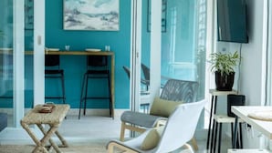 Une chambre moderne avec des murs de couleur turquoise, un ventilateur de plafond, un téléviseur à écran plat, une table à manger avec des chaises et une plante en pot.
