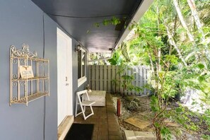 A covered outdoor area with a metal shelf, a white chair, and a wooden bench. - Peacock 2 in Fort Lauderdale (Fort Lauderdale)