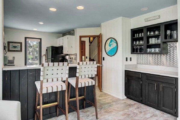 A kitchen with dark cabinets, a white countertop, and two white bar stools with brown accents.