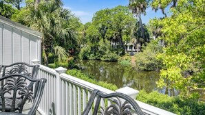 A white building with a balcony overlooking a pond surrounded by lush greenery and tall trees. - Award-Winning Resort Amenities | Racquet Club Villa 37 (Isle of Palms)