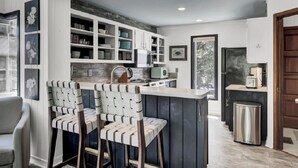 A modern kitchen with white cabinetry, a central island with bar stools, and a built-in microwave. - Award-Winning Resort Amenities | Racquet Club Villa 37 (Isle of Palms)