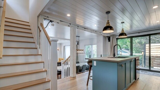 A modern kitchen with a central island, wooden staircase, and large windows. - 3-bedroom house 915A Shefford mountain view (Bromont)