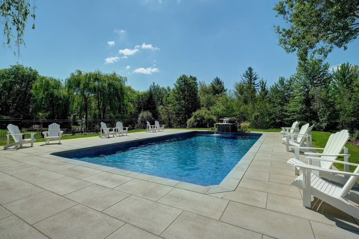 Ein rechteckiger Pool mit Wasserfall, umgeben von weißen Liegestühlen und einer gepflasterten Terrasse.