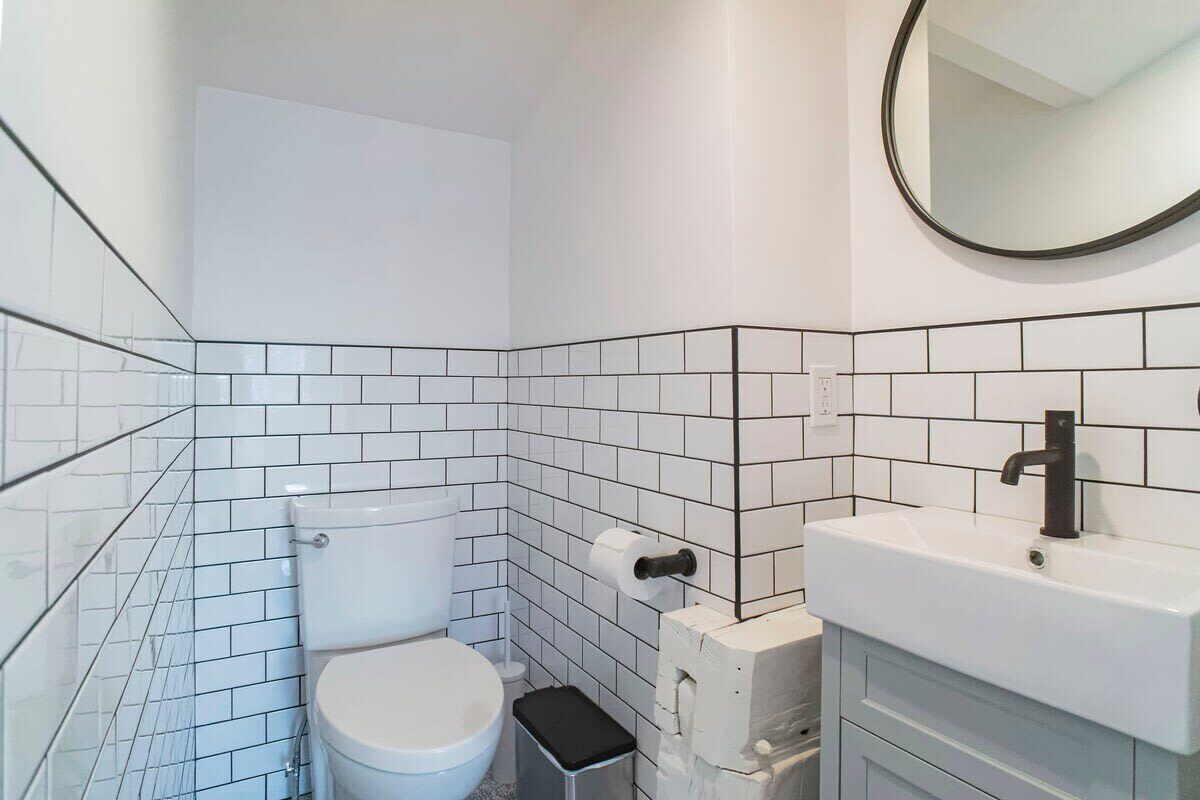 Ein Badezimmer mit weißen Fliesen, einer Toilette, einem Waschbecken und einem Spiegel.