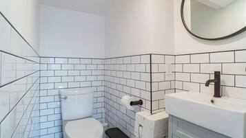Ein Badezimmer mit weißen Fliesen, einer Toilette, einem Waschbecken und einem Spiegel.