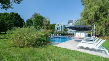 A swimming pool with lounge chairs, a covered area, and a house in the background.